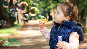 A young girl wearing a winter coat plays with bubbles, looking fully involved and intent on her activity.