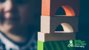A young boy, shown in soft focus, peers out from a fort made of blocks he has built.