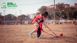 A mother guides her child while playing ball in the middle of a field with a dry patch of grass.