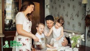 A mother and father playfully teach their children how to bake in a sunny kitchen, creating a happy and content atmosphere.