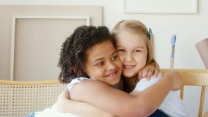 Two young girls hugging each other while participating in ABA therapy, enjoying activities and learning to be friends.