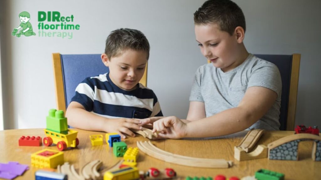 Two boys play on a table with toy trains, sharing and enjoying a happy, content moment during a DIR/Floortime session.