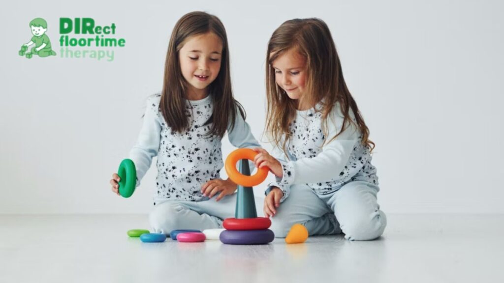 Two young girls share a bonding moment, playing with plastic donut toys and a cone during a DIR/Floortime session.