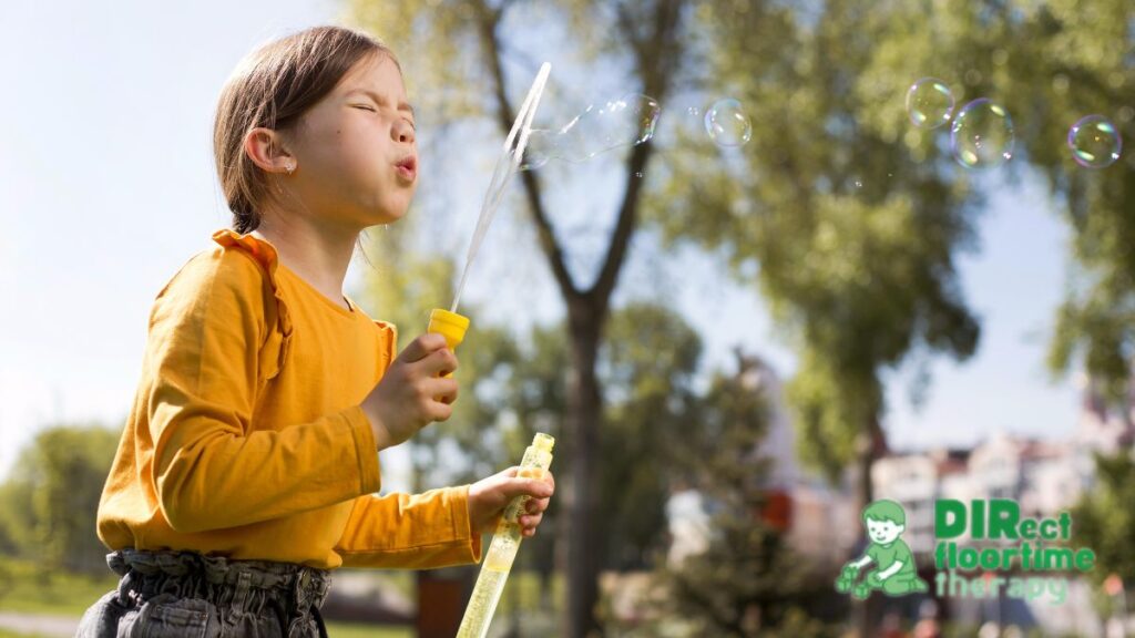 A young girl plays with bubbles in a field, focused and engaged as she works toward her goal of blowing large bubbles through the DIR Floortime model.