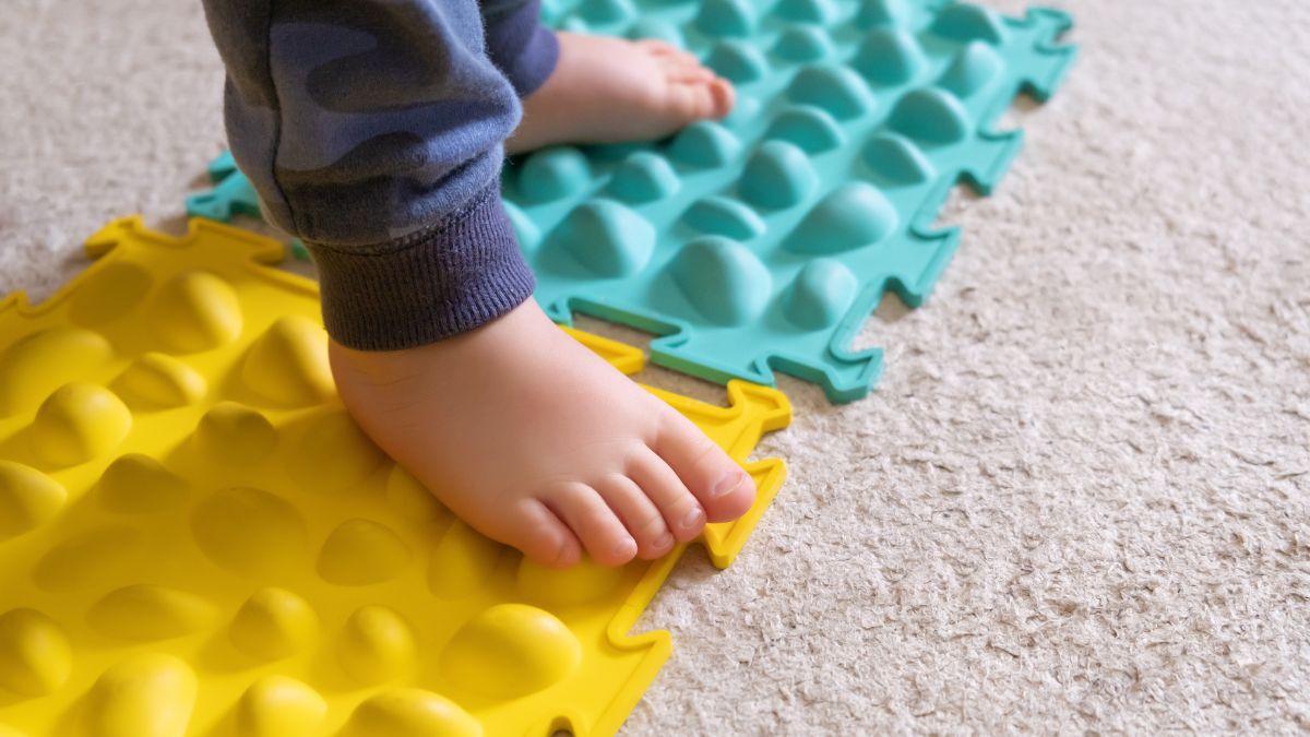 A young child with autism presses his foot on a sensory tactile board as part of a sensory diet activity.