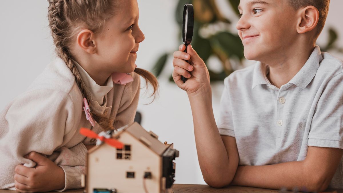 A young boy holds a magnifying glass up to a female peer, who smiles and enjoys the playful exchange, illustrating DIR Floortime interaction.