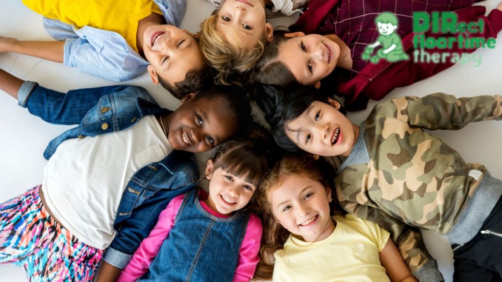 A group of children lie on the floor in a circle, looking up at the camera and smiling during a DIR Floortime speech therapy session.