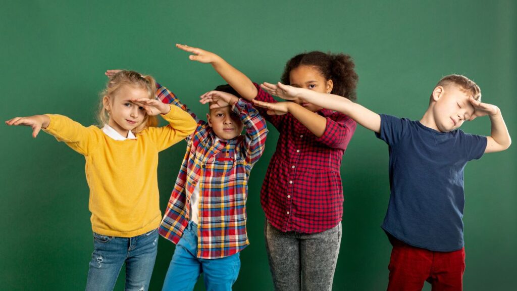 A row of children on a green background raise their arms to the left during a movement play activity.