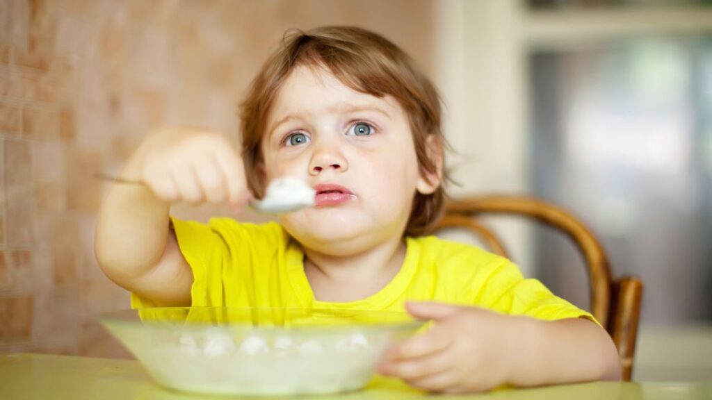 Picky eater autism, a young female toddler frustrated while lifting a spoon from a cereal bowl.