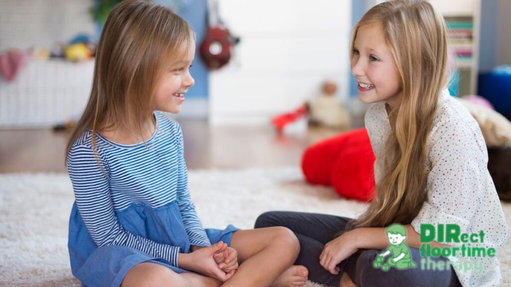 Two young girls sit together on a sofa, talking and sharing interests.