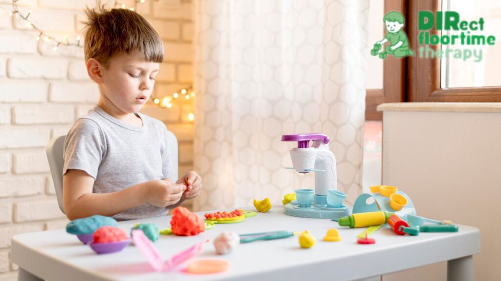 A young boy arranges small items on a white table to place in a sensory bin.