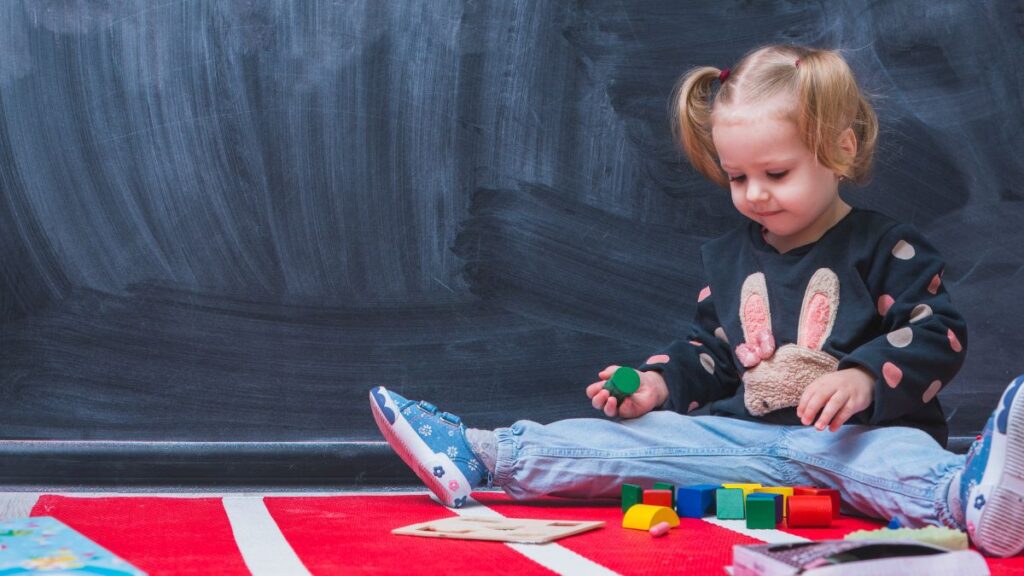 School readiness autism, a young girl engaged in floor play in a room with a dark curtain backdrop.