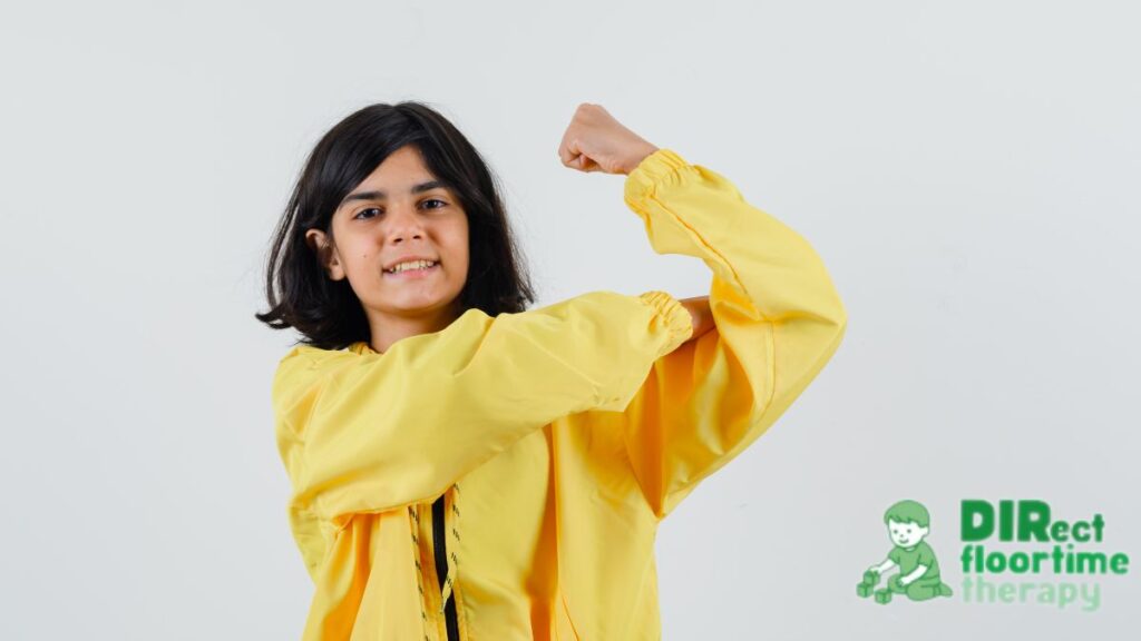 A young girl wearing a yellow pullover raises her arm, showing confidence and strength.