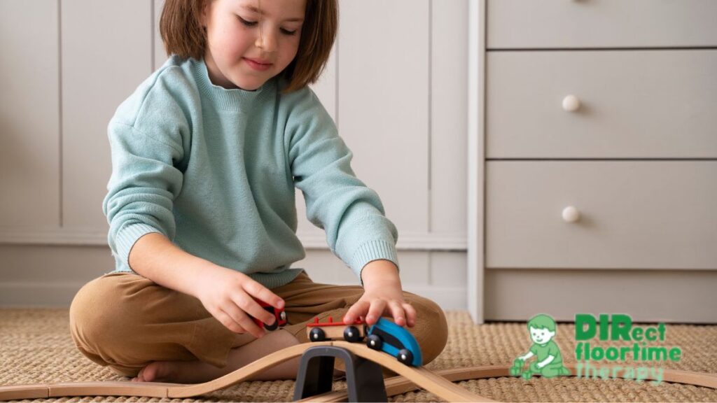 A young girl sits on the floor smiling while playing with her toy trains.