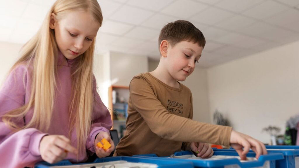 Two children, a boy and a girl, arrange small items and materials to create a sensory bin for a hands-on play project.