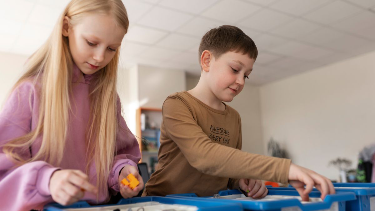 Two children, a boy and a girl, arrange small items and materials to create a sensory bin for a hands-on play project.