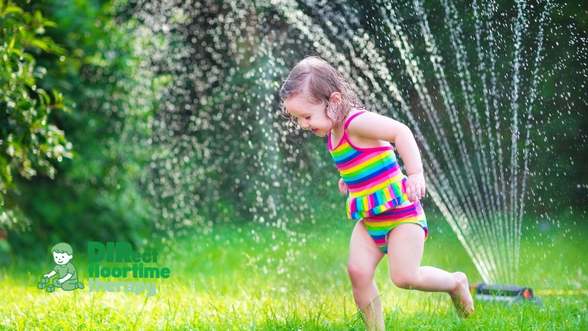 Young child happily playing through a backyard sprinkler during summer as a sensory-friendly outdoor activity for autistic children, supported by DIRFloortime therapy in New Jersey.
