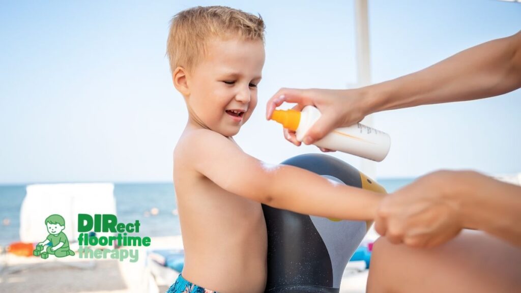 Swimming, Sunscreen, and Sprinklers: Sensory-Safe Summer Activities for Autistic Children in NJ 1 Parent gently applying sunscreen to a young autistic child before a beach or pool outing using sensory-friendly strategies recommended through DIRFloortime therapy in New Jersey.