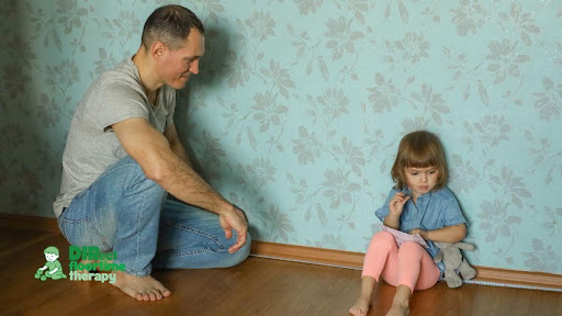 A parent maintaining calm, grounded presence beside a distressed child on the floor, neither restraining nor punishing