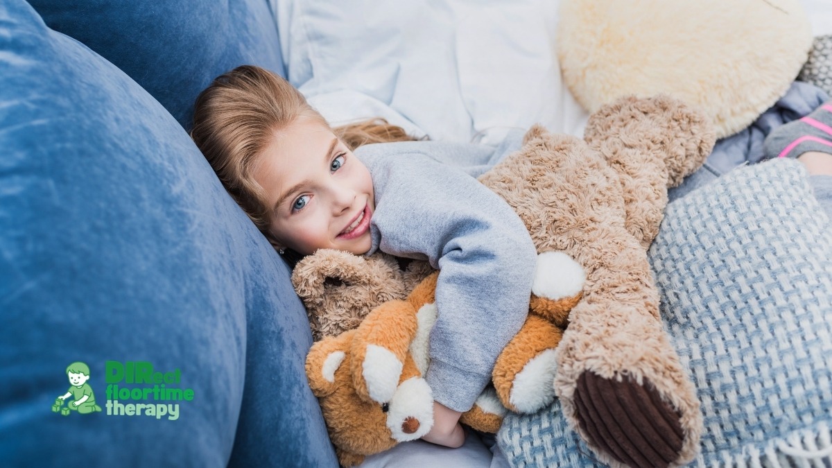 A child lying in a softly lit bedroom, looking calm and comfortable, with a weighted blanket and familiar stuffed animals nearby