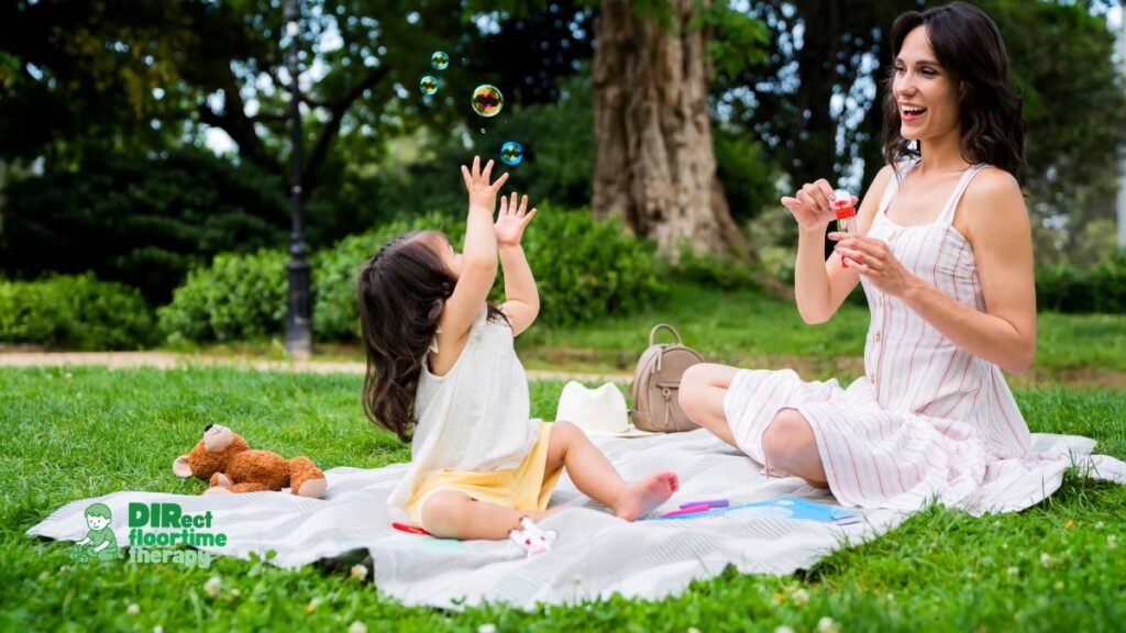 A child and parent engaged in bubbles play, both watching the same bubble, the child glancing at the parent with delight capturing a joint attention moment: 'parent children  bubbles joint attention autism joyful home NJ'