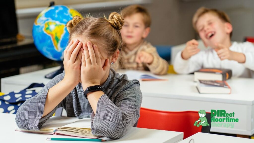 Sensory Overload at School: How to Spot the Signs in Your Autistic Child Before It Becomes a Crisis 1 A child sitting at a school desk with hands pressed over ears, eyes closed, surrounded by a blurred classroom environment suggesting noise and movement : autistic child school desk hands over ears sensory overwhelm classroom