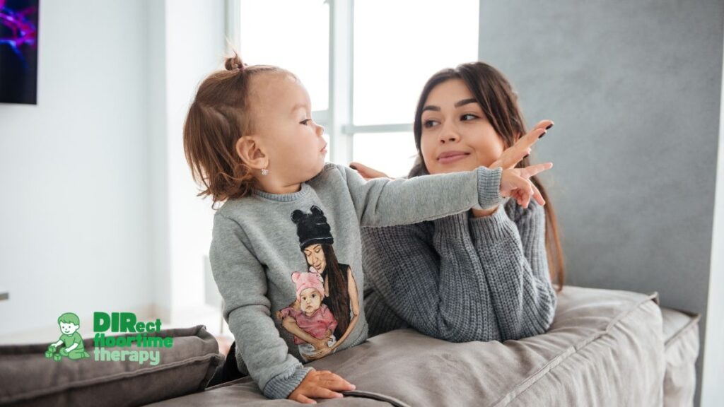 A parent and child sitting together watching a favourite show, the child pointing at the screen and making eye contact with the parent, showing communicative intent: 'parent child watching show together autistic child pointing communicative'-'Echolalia '