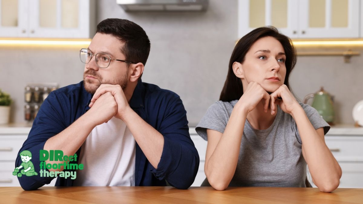 A couple sitting together at a kitchen table after a difficult day, both looking tired but connected, hands touching, conveying exhaustion and partnership simultaneously:'couple kitchen table tired connected autism parenting partnership NJ'