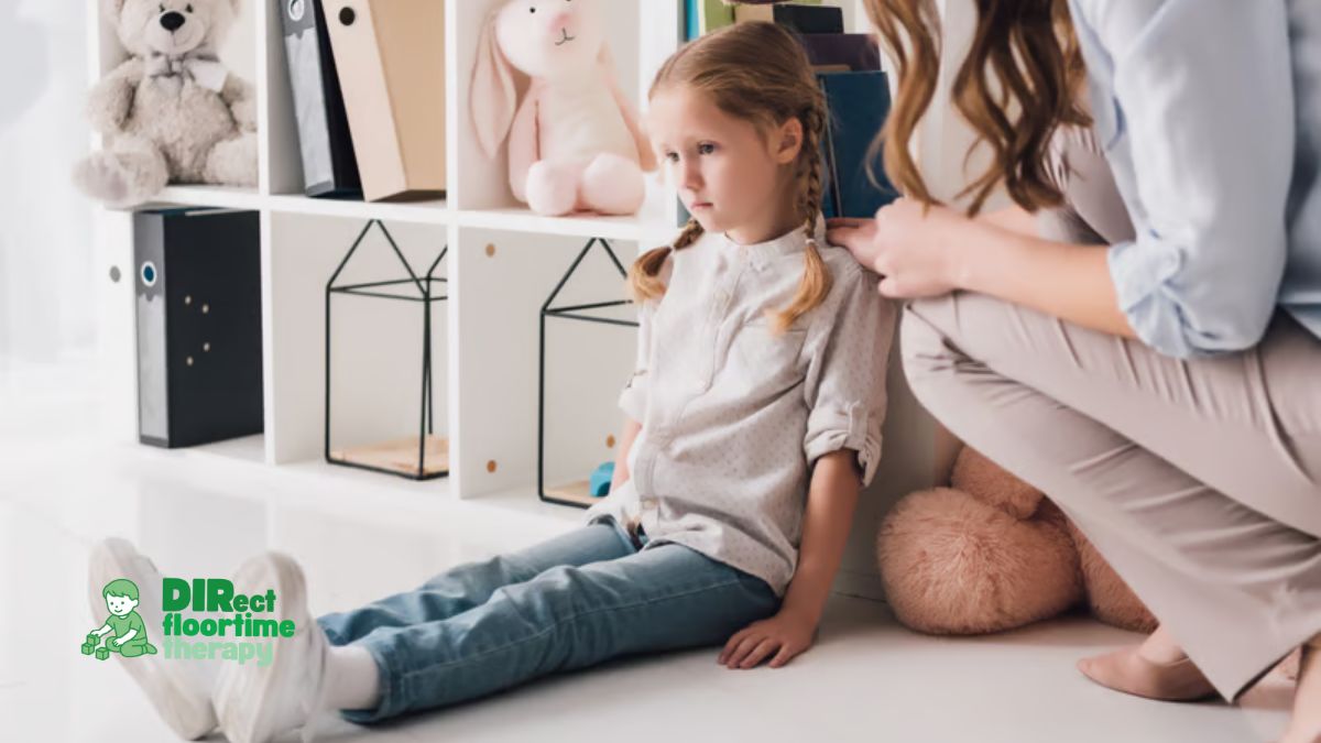 A child sitting on the floor with arms crossed and head turned away, a parent nearby kneeling at the child's level with a calm, open expression, not forcing engagement autistic child demand avoidance refusal parent calm presence NJ home